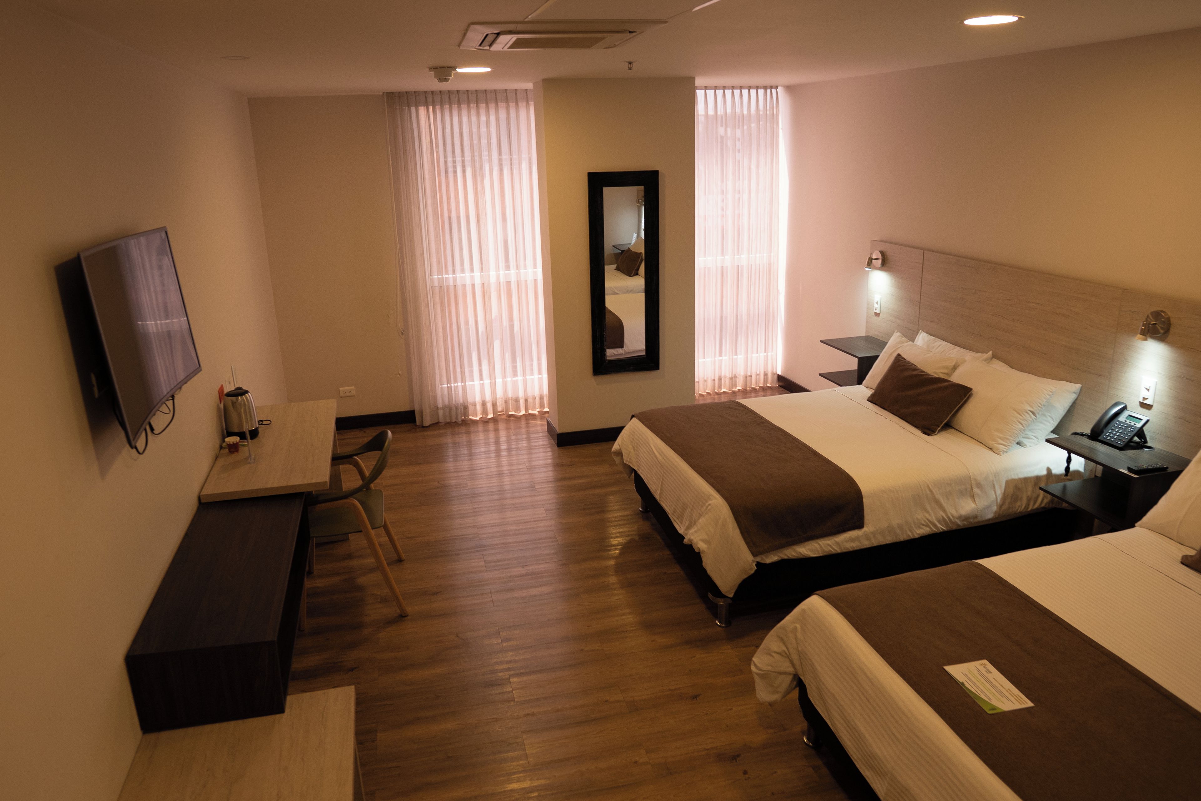 A hotel room with two beds, a desk, a chair, a TV, and a mirror.