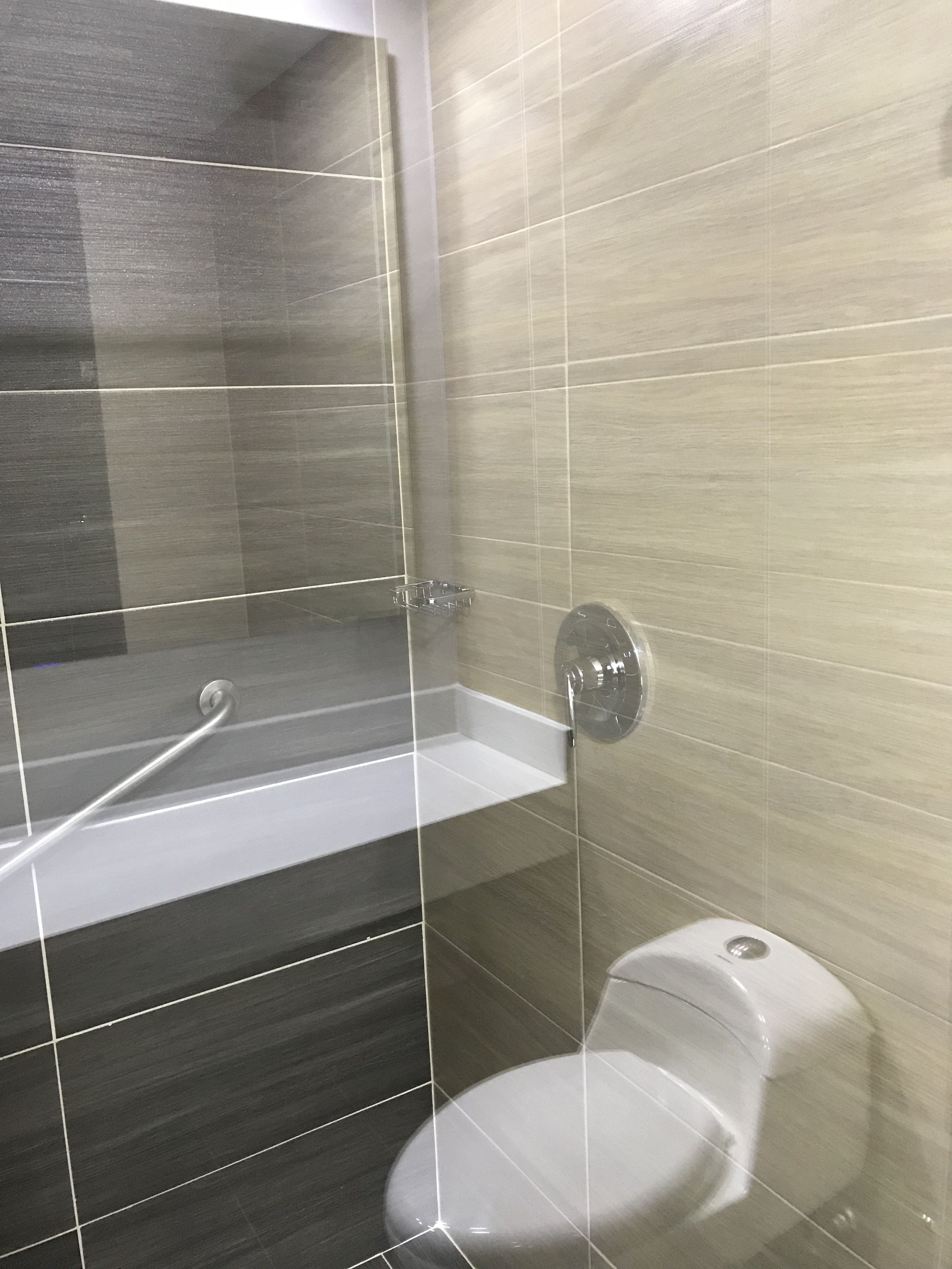 Un baño moderno con ducha de mampara de vidrio, inodoro blanco y pared revestida de baldosas oscuras.