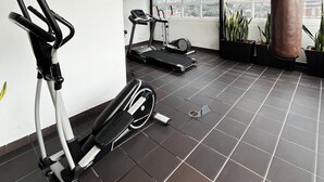 Un gimnasio con equipo de ejercicio, un saco de boxeo y vistas a la ciudad a través de amplias ventanas.