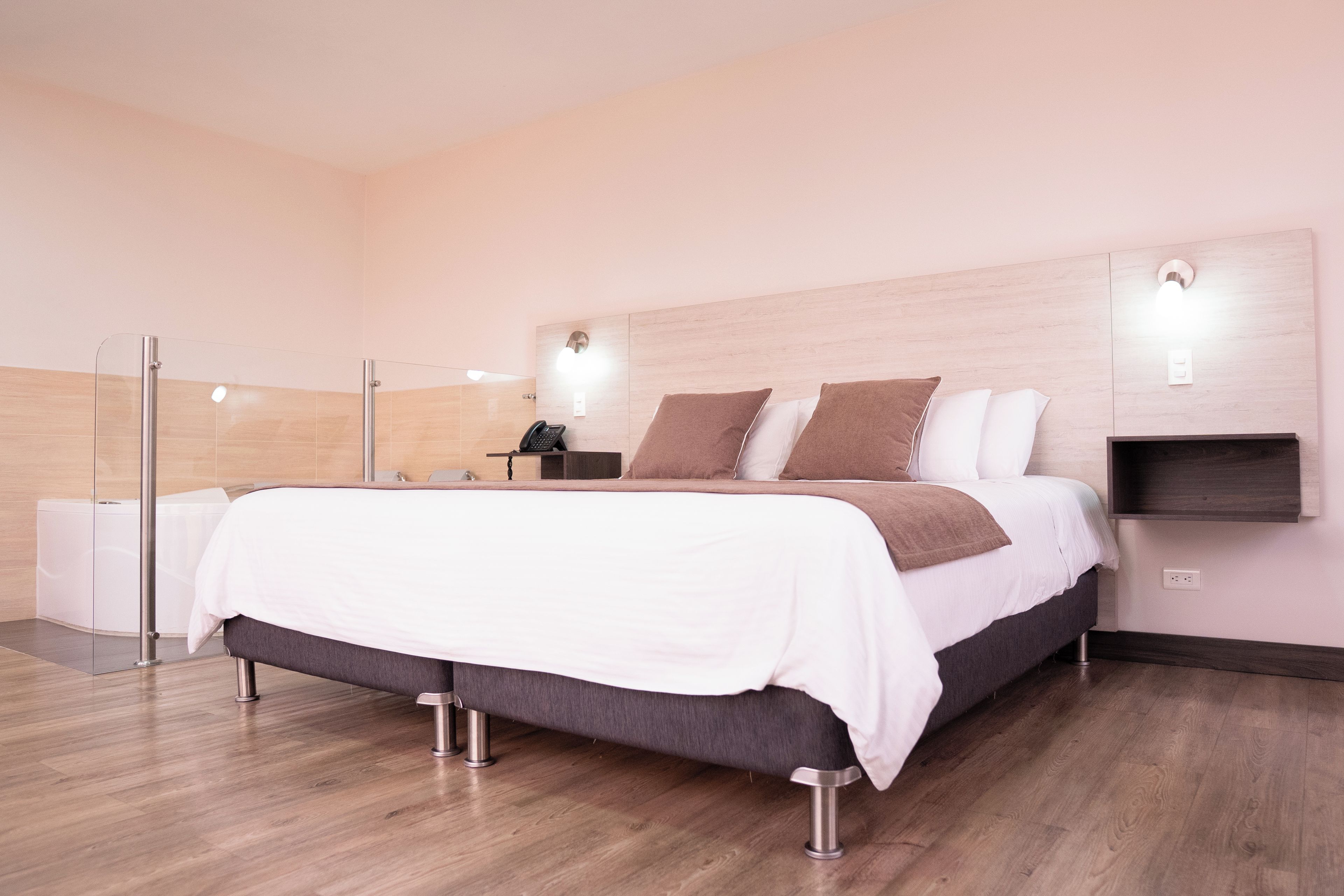 Ett modernt hotellrum med en stor säng, sängbord, en dusch och ett trägolv.