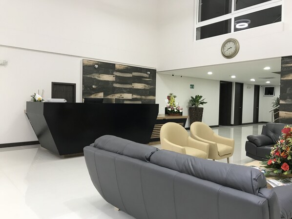 A modern reception area with a black reception desk, beige chairs, and a grey sofa. - Arame Hotel (Envigado)