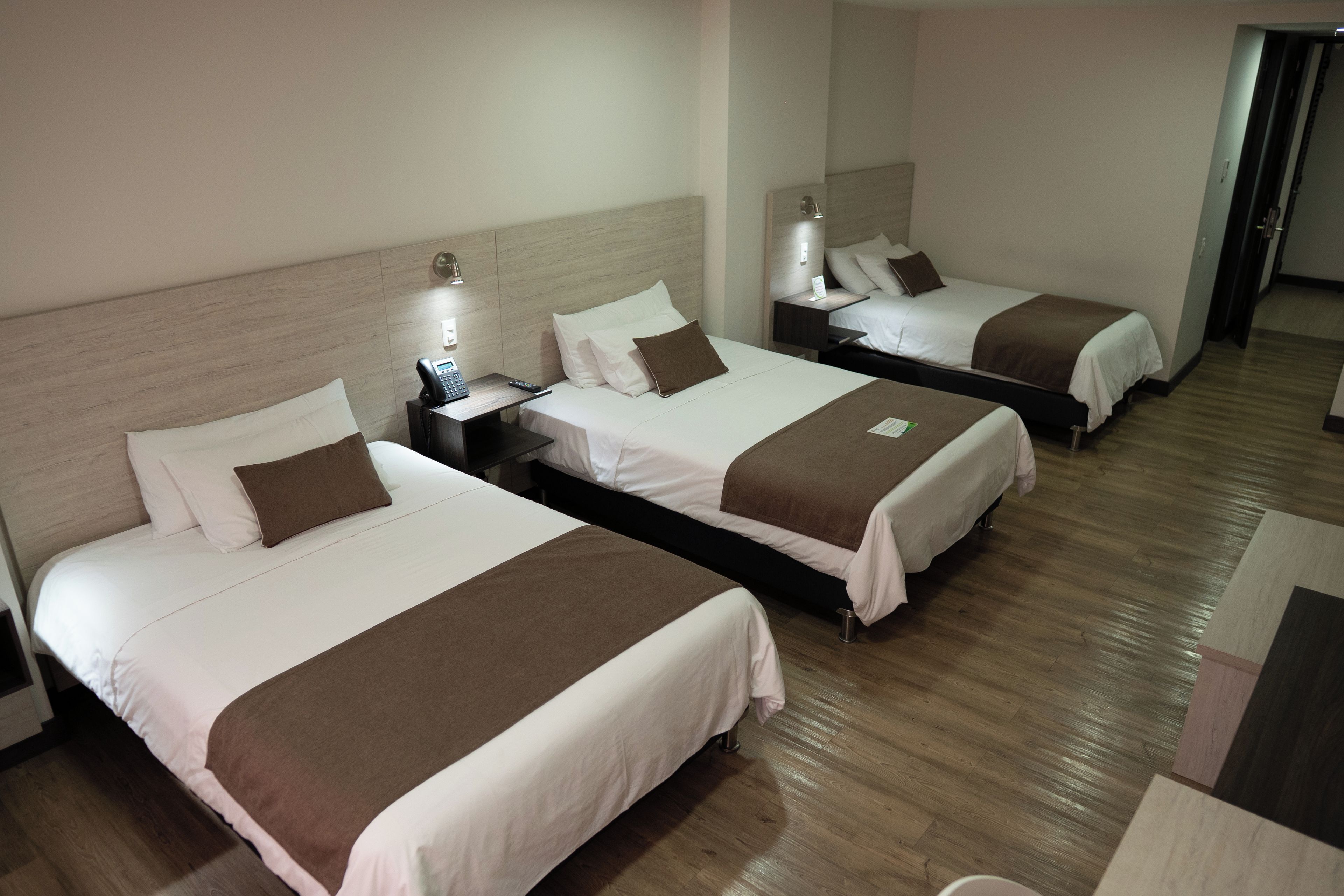 A hotel room with three beds, each with a bedside table and lamp.