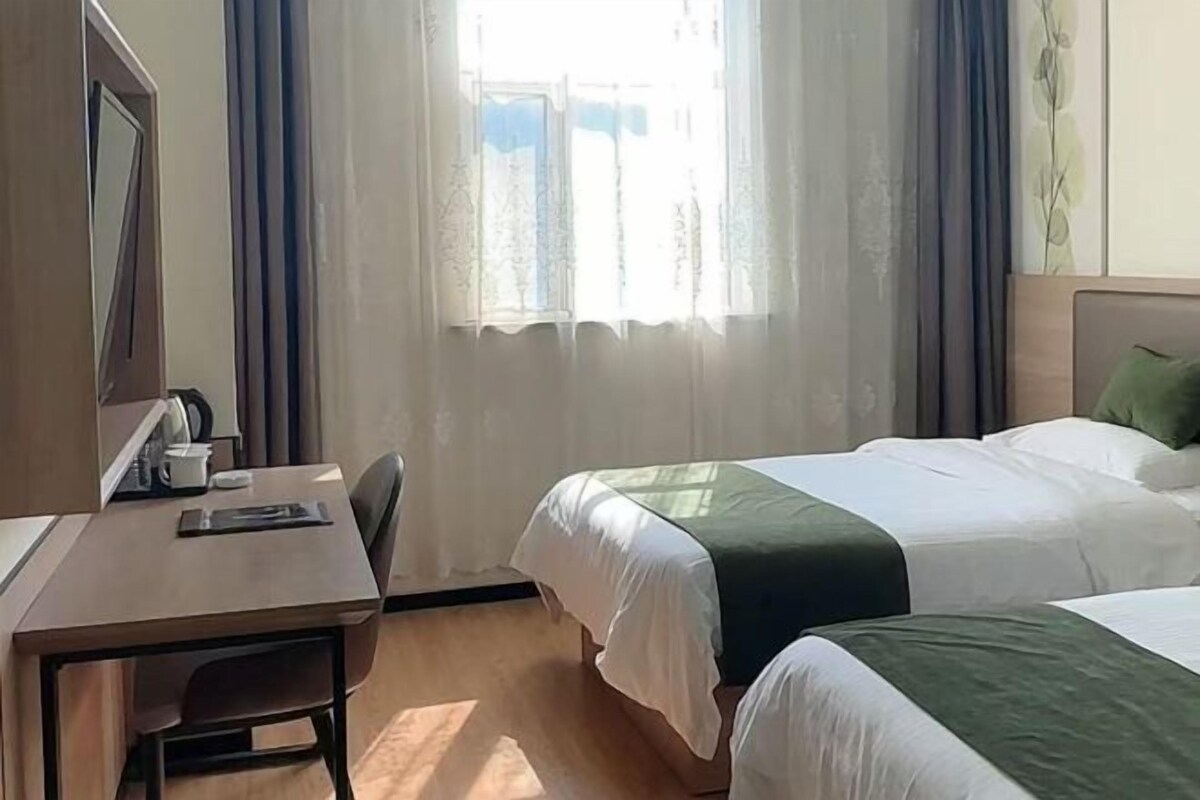 Habitación de hotel con dos camas, un escritorio, una silla y un ventanal con cortinas.