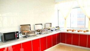 A kitchen with red cabinets, a microwave, and a buffet setup with various food items. - GreenTree Inn Suzhou Zhangjiagang Daxin Town Pingbei Road Express Hotel (Suzhou)
