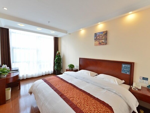A hotel room with a large bed, a desk, a telephone, and a window with curtains.