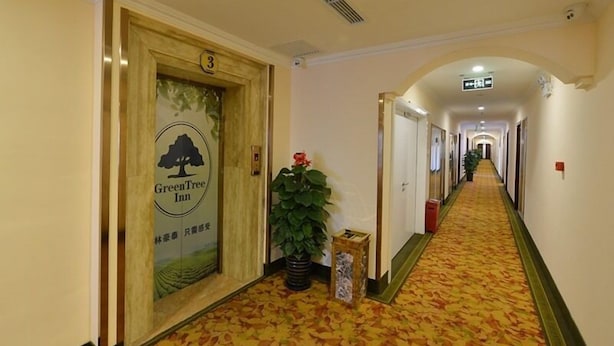 A hotel hallway with a carpeted floor, a reception desk, and a sign for the GreenTree Inn. - GreenTree Inn BeiJing Haidian Shijingshan N Univ of Tech Htl (Beijing)