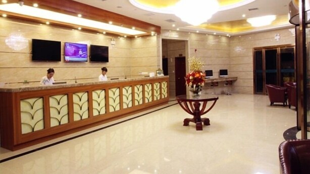 A hotel reception area with a reception desk, two receptionists, a large chandelier, and a seating area with chairs. - GreenTree Inn Prov. Suzhou Wuzhong Fengjin Rd Business Hotel (Suzhou)