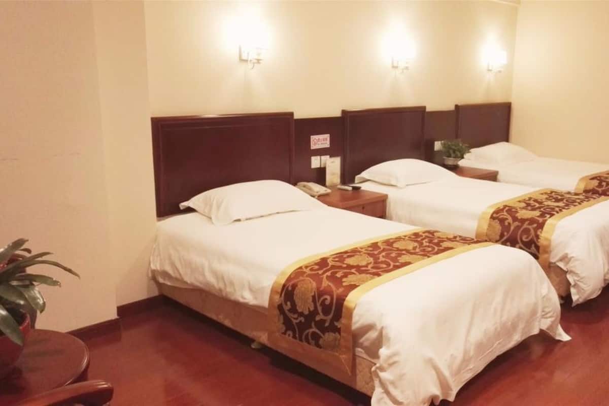 Une chambre d’hôtel avec deux lits simples, des têtes de lit en bois, du linge de lit blanc et une petite table de chevet avec une lampe.