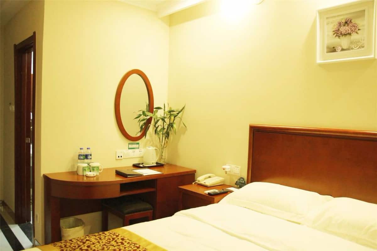 Une chambre d’hôtel avec un lit, un bureau en bois avec un téléphone, un miroir et une petite plante.
