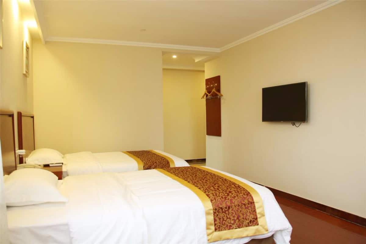 Une chambre d’hôtel avec deux lits, un téléviseur à écran plat fixé au mur et un plancher en bois.
