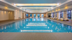 Une grande piscine intérieure à l’eau d’un bleu cristallin, entourée de chaises longues et dotée d’un design de plafond moderne.