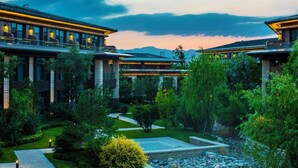 Un hôtel moderne composé de plusieurs bâtiments, doté d’un jardin bien entretenu et offrant une vue dégagée sur les montagnes en arrière-plan.