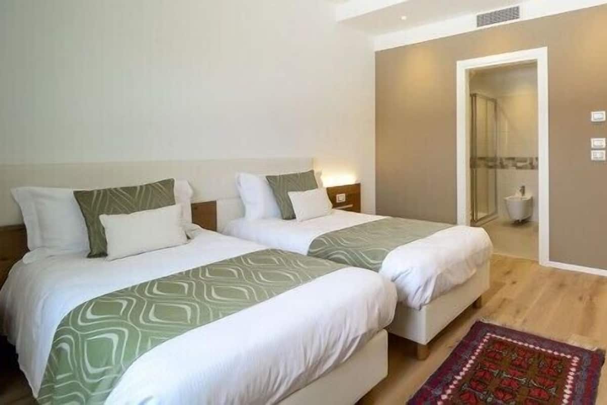 Une chambre d’hôtel avec deux lits, un plancher en bois, une petite salle de bain et un bureau avec une lampe.
