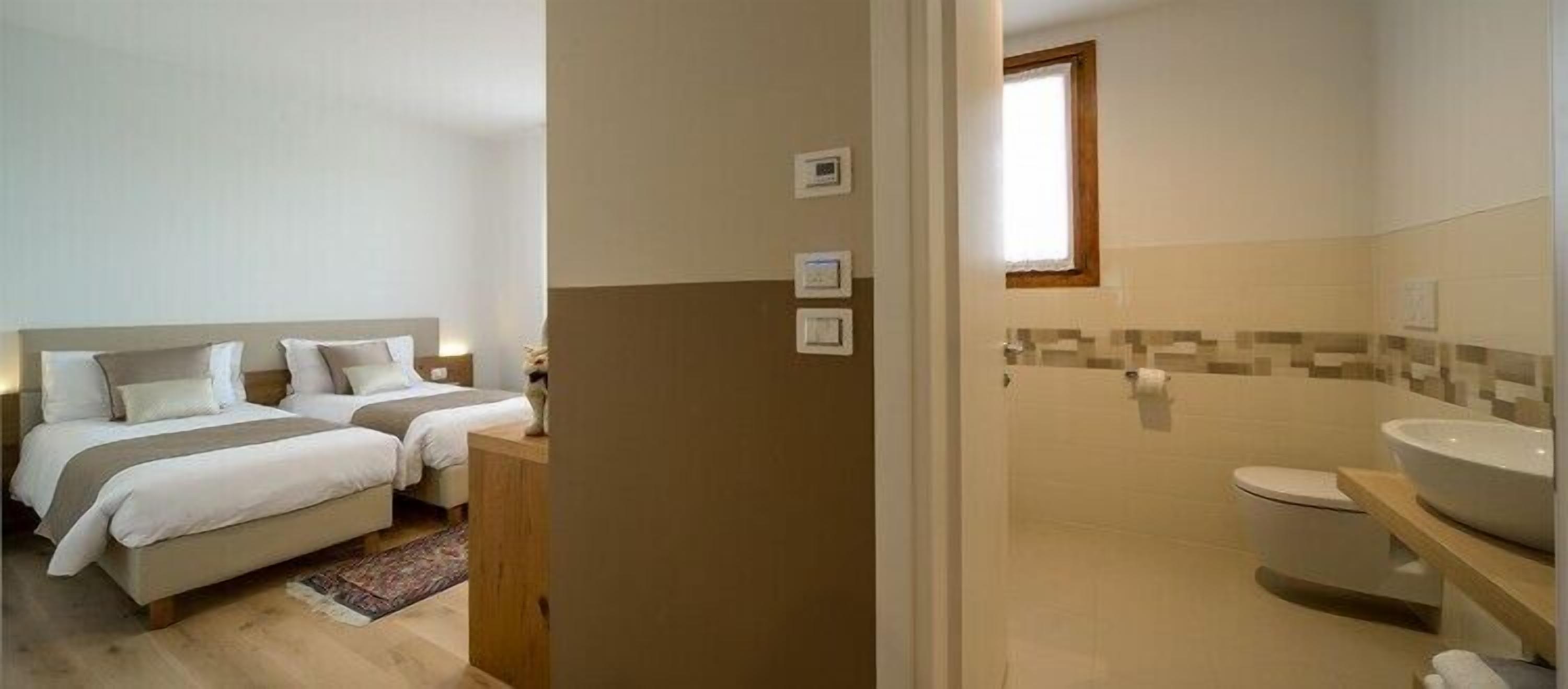 Un dormitorio con dos camas, un baño con lavamanos e inodoro, y una ventana pequeña.