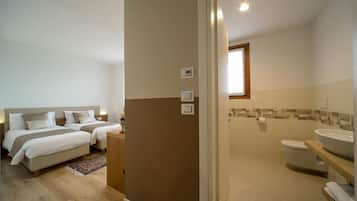 Ein Schlafzimmer mit zwei Betten, ein Badezimmer mit Toilette und Waschbecken sowie einer Dusche.