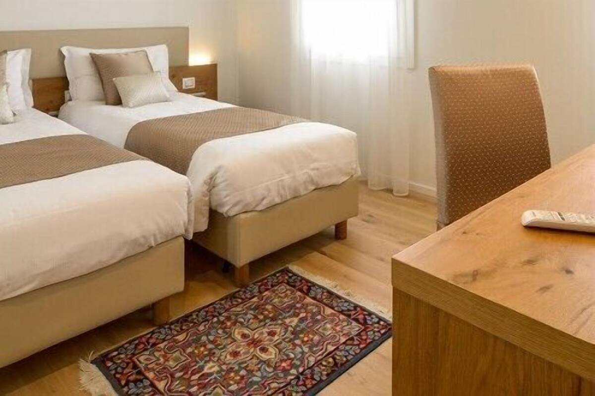 Une chambre d’hôtel avec deux lits, un bureau en bois et un tapis à motifs.