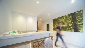 Un área de recepción moderna con un mostrador blanco, un elemento de pared de piedra y un mural grande con motivos naturales.