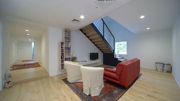 A modern living room with a staircase, a red sofa, and a TV on a white shelf.
