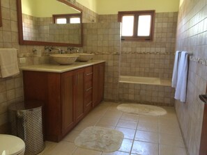 A bathroom with two sinks, a mirror, a window, a toilet, and a trash can. - Villa Jacaranda Sosua (Sosúa)