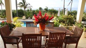 A wooden table with six chairs and a potted plant with red flowers. - Villa Jacaranda Sosua (Sosúa)