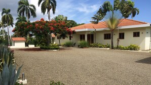 A building with a red-tiled roof, surrounded by gravel and palm trees. - Villa Jacaranda Sosua (Sosúa)