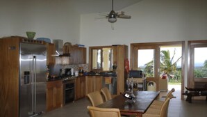 A modern kitchen with a dining area, wooden cabinets, a stainless steel refrigerator, and a view of the outdoors. - Villa Jacaranda Sosua (Sosúa)