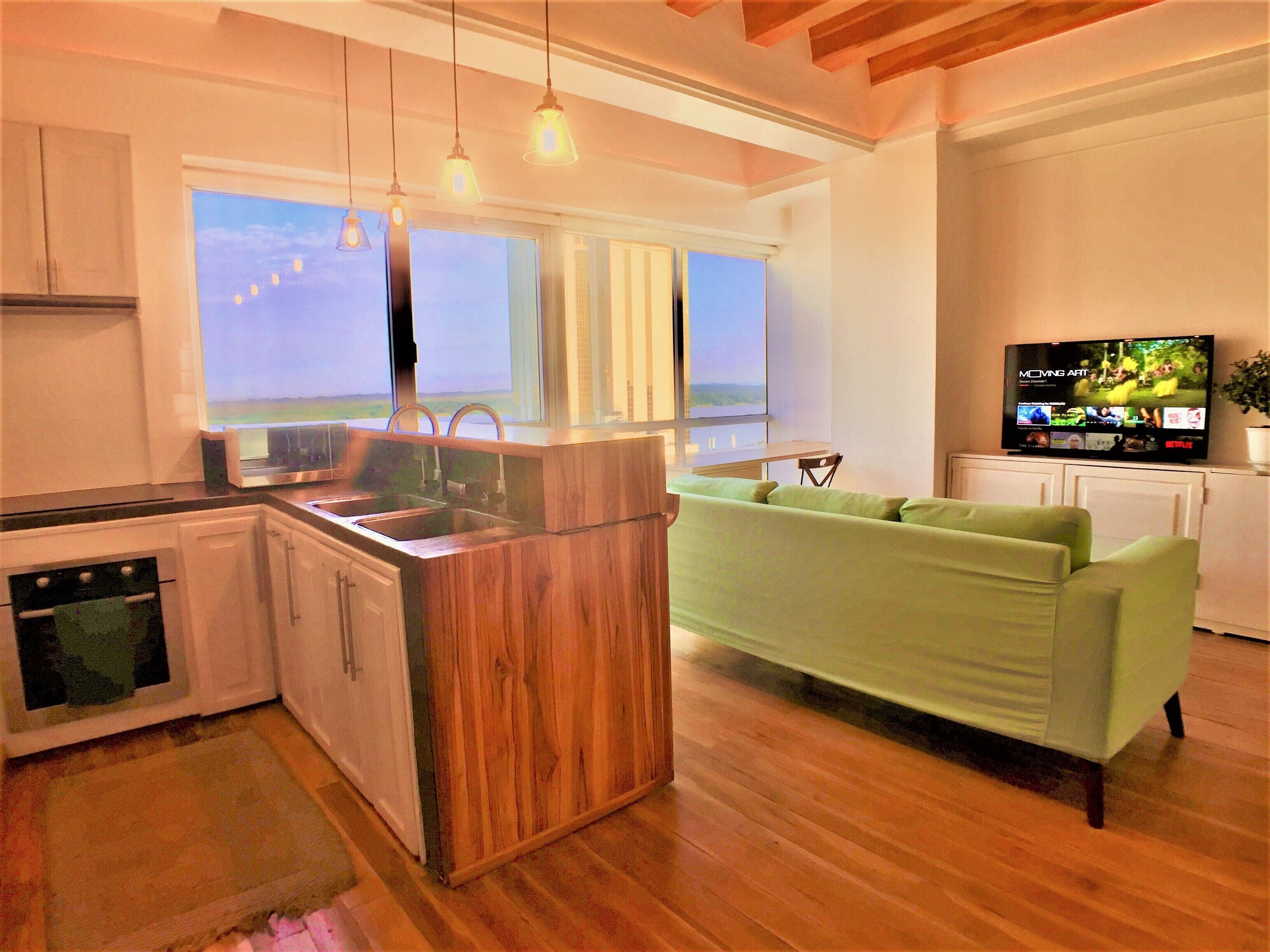 A modern kitchen with a wooden island, a green sofa, and a TV displaying a movie.