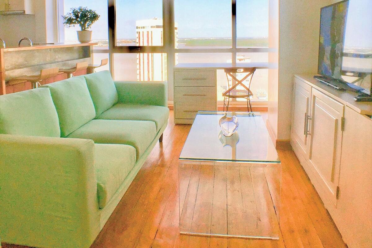 A modern living room with a green sofa, wooden flooring, a glass coffee table, and a TV on a cabinet.