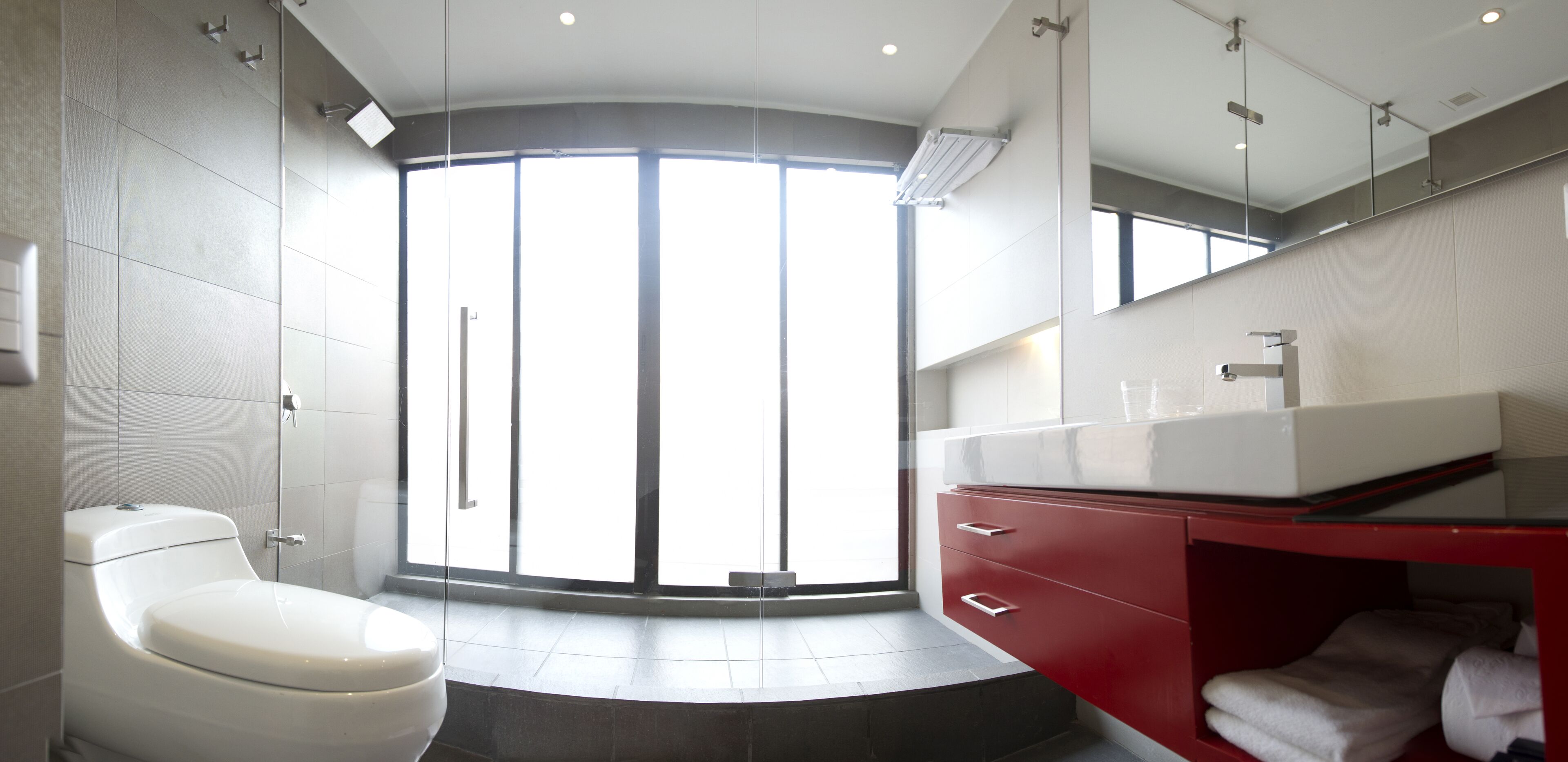 Une salle de bain moderne comprenant des toilettes, un meuble-lavabo avec un miroir et une grande fenêtre laissant entrer la lumière naturelle.