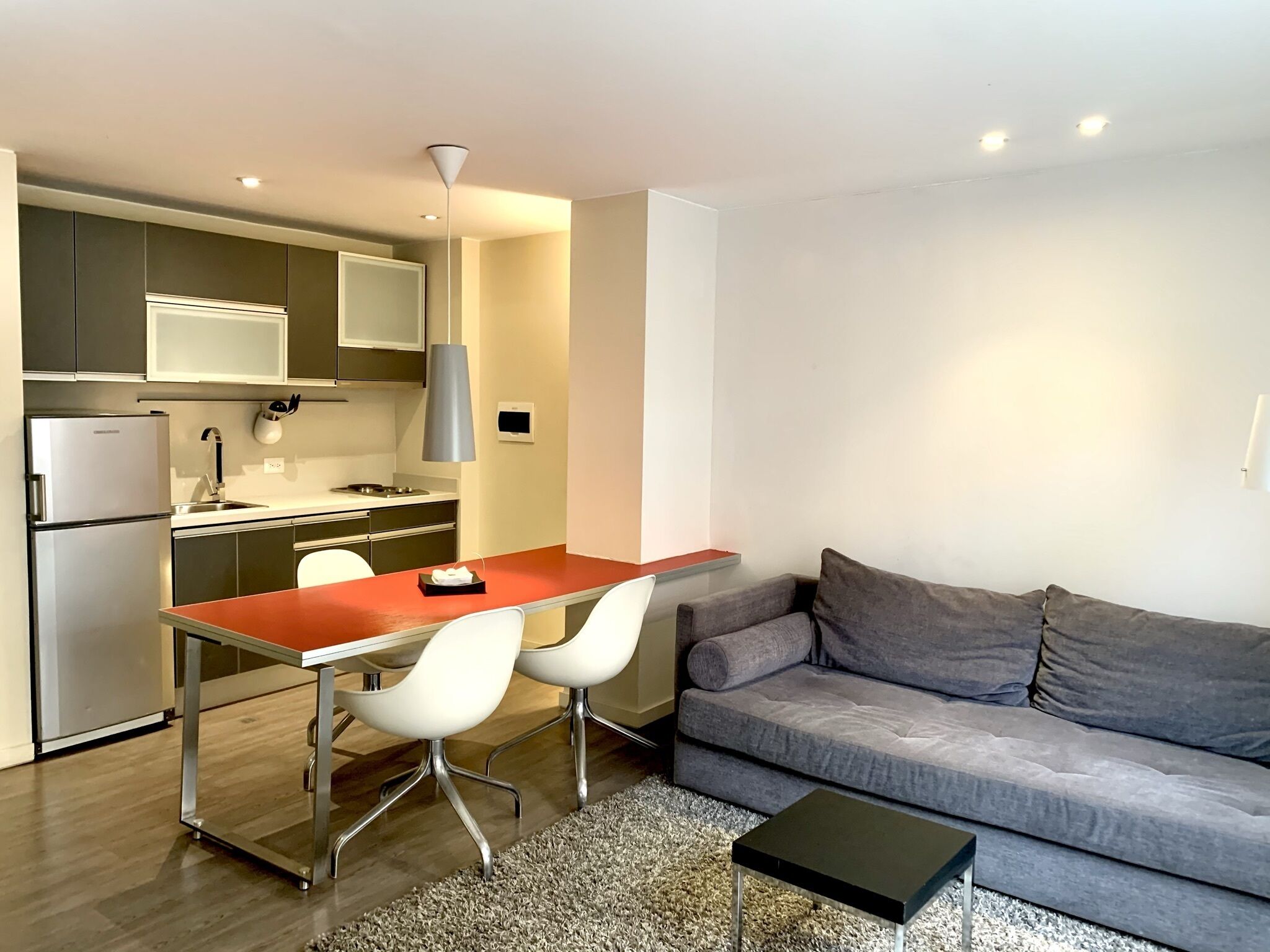 A modern kitchen with a dining area, a grey sofa, and a small black table.
