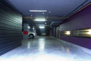 A parking garage with a white car parked in the distance, fluorescent lighting, and a purple wall. - Central Apartamentos Bogota (Bogotá)