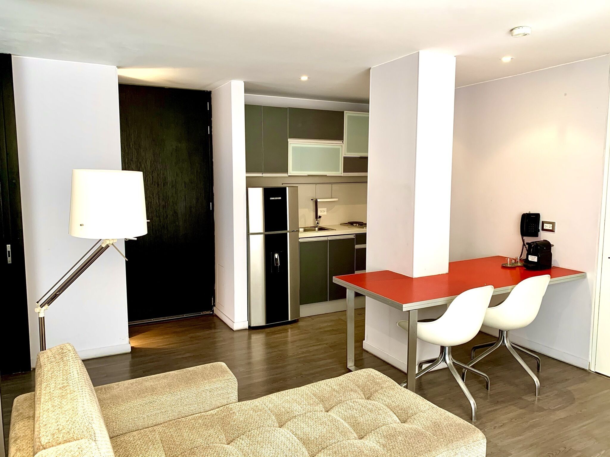 A compact living space with a kitchenette, a dining area with two chairs, a sofa, and a floor lamp.
