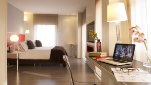 A hotel room with a bed, desk, chair, lamp, laptop, books, and a vase with flowers. - Central Apartamentos Bogota (Bogotá)