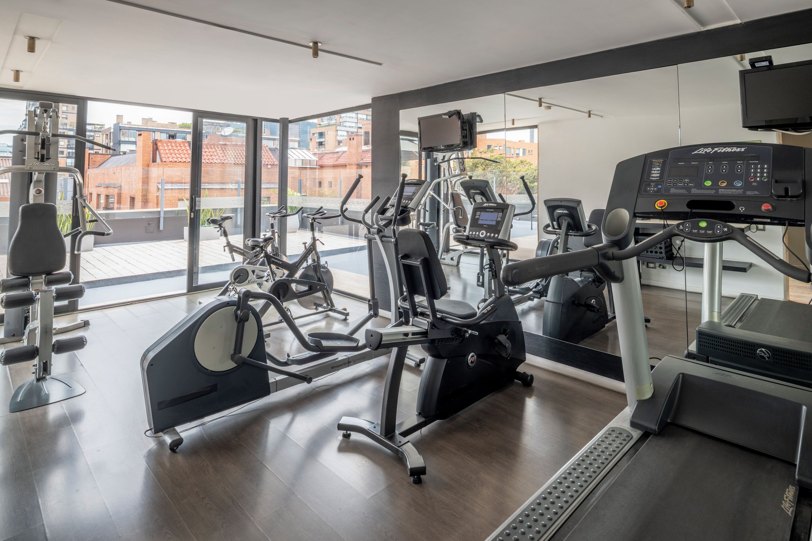 Ein modernes Fitnessstudio mit verschiedenen Trainingsgeräten, großen Fenstern und Blick auf Gebäude außerhalb.