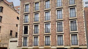 A multi-story building with a brick facade, multiple windows with black railings, and a central entrance with a garage. - Central Apartamentos Bogota (Bogotá)