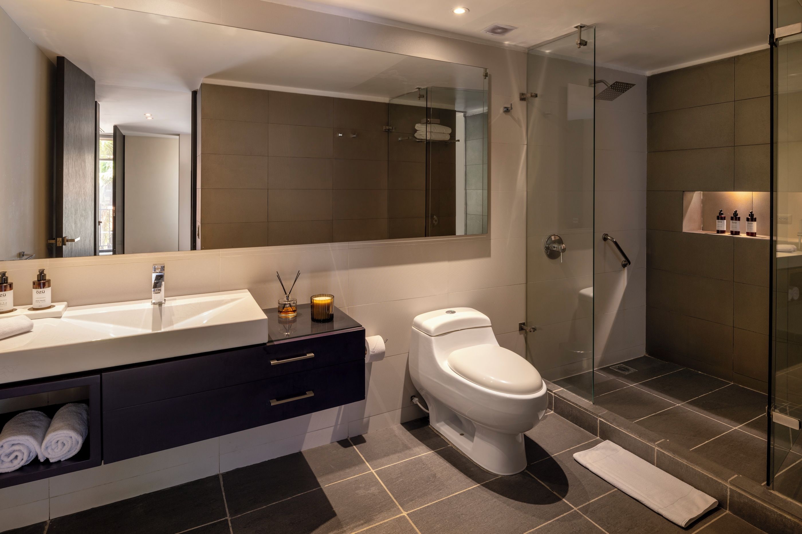 A modern bathroom with a large mirror, a white sink, a dark vanity, a toilet, and a glass-enclosed shower area.