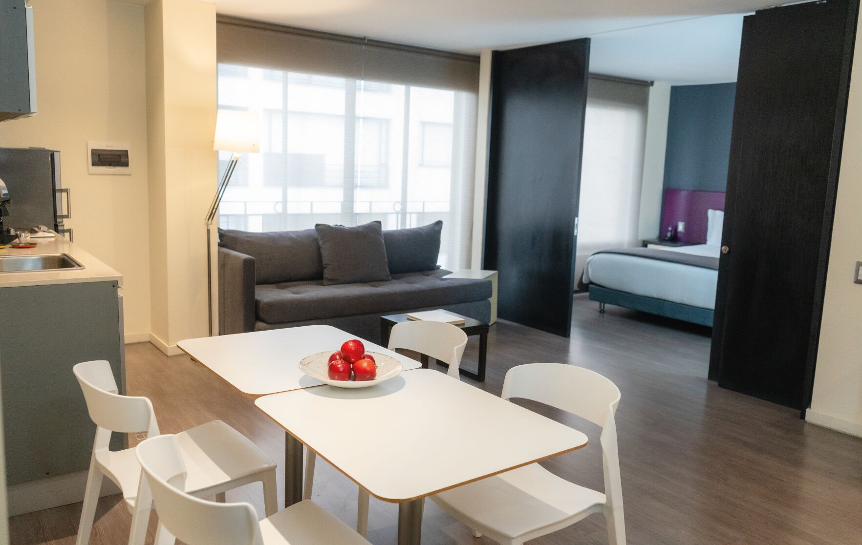 Un espace de vie moderne et bien éclairé, comprenant un canapé, une table à manger avec des chaises, et un coin cuisine avec un évier et un plan de travail.