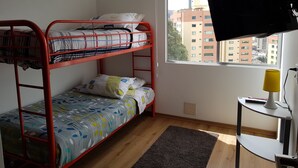 Ein Schlafsaalzimmer mit Etagenbetten, einem Fenster mit Blick auf Gebäude, einem Schreibtisch mit Lampe und einer Steckdose.