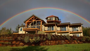 A large house with a prominent balcony and a tower, surrounded by a landscaped garden with rocks and plants. - Bella Collina Bed & Breakfast (Amity)
