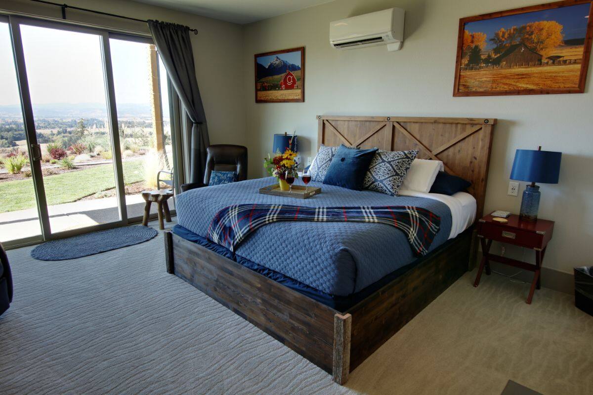 Een slaapkamer met een groot bed, een houten hoofdeinde, een nachtkastje met een lamp en uitzicht op de omgeving door een schuifdeur.