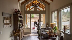 A spacious room with a high ceiling, wooden beams, and large windows. There is a chandelier, a fireplace, and a cozy seating area with a rug. - Bella Collina Bed & Breakfast (Amity)