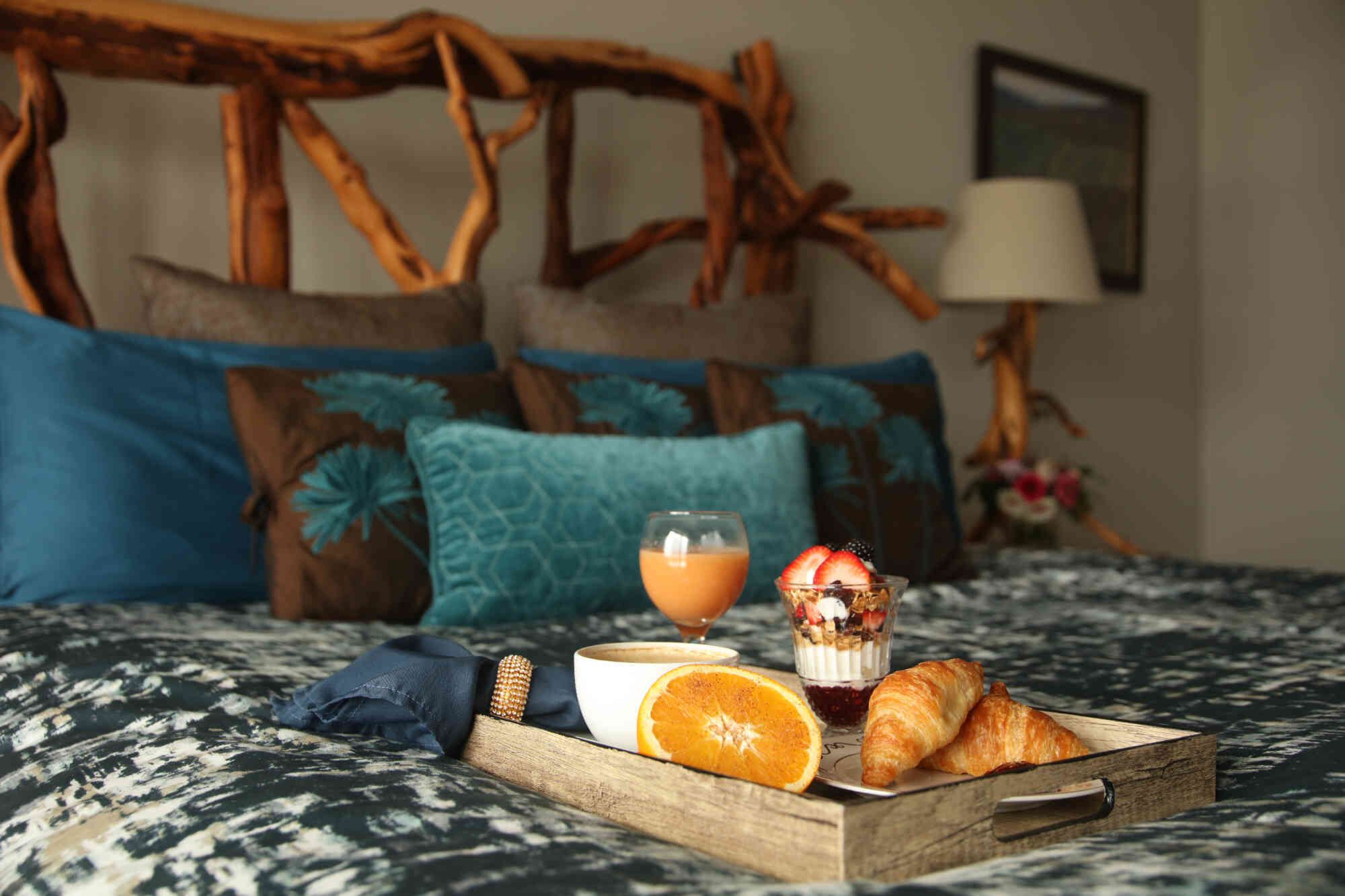 A bed with a wooden headboard, a tray with croissants, a glass of orange juice, and a bowl of cereal.