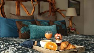 A bed with a wooden headboard, a tray with croissants, a glass of orange juice, and a bowl of cereal.