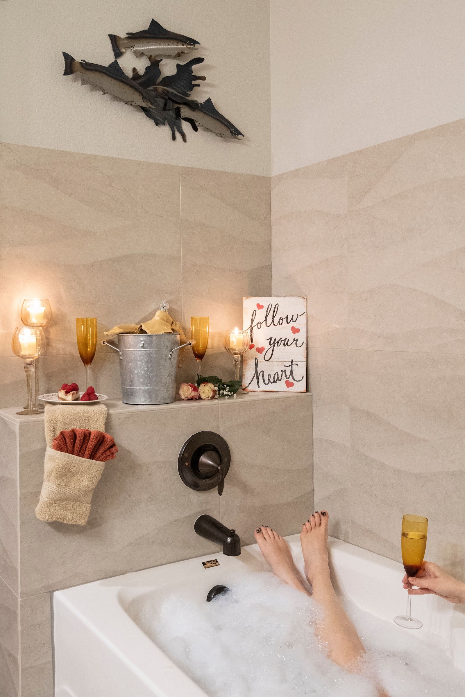 A bathtub with a person relaxing, surrounded by amenities like candles, a sign, and decorative items.