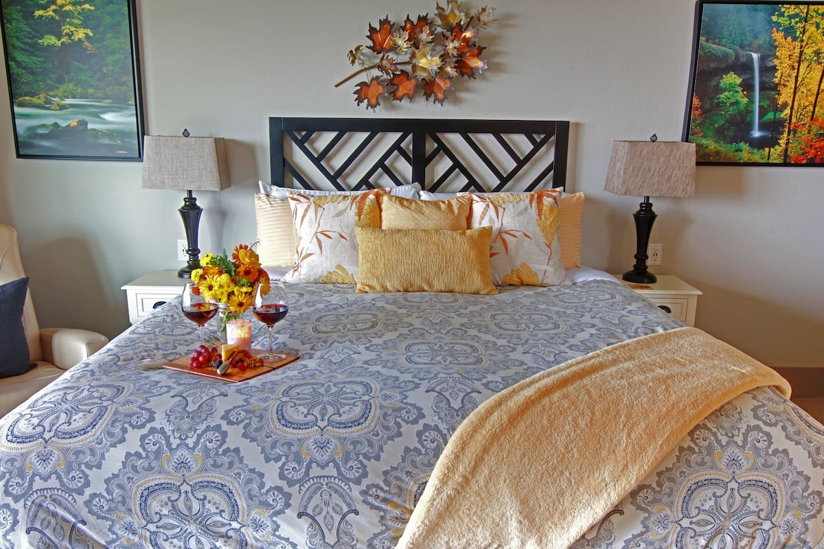 Een net opgemaakt bed met een bedsprei met een patroon, twee bedlampen, een decoratief wandobject en een ingelijst schilderij boven het bed.