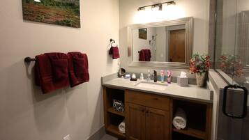 Une salle de bain avec un lavabo blanc, un meuble-lavabo en bois et un miroir au-dessus. Des serviettes rouges sont suspendues à des crochets et un tableau encadré est accroché au mur.