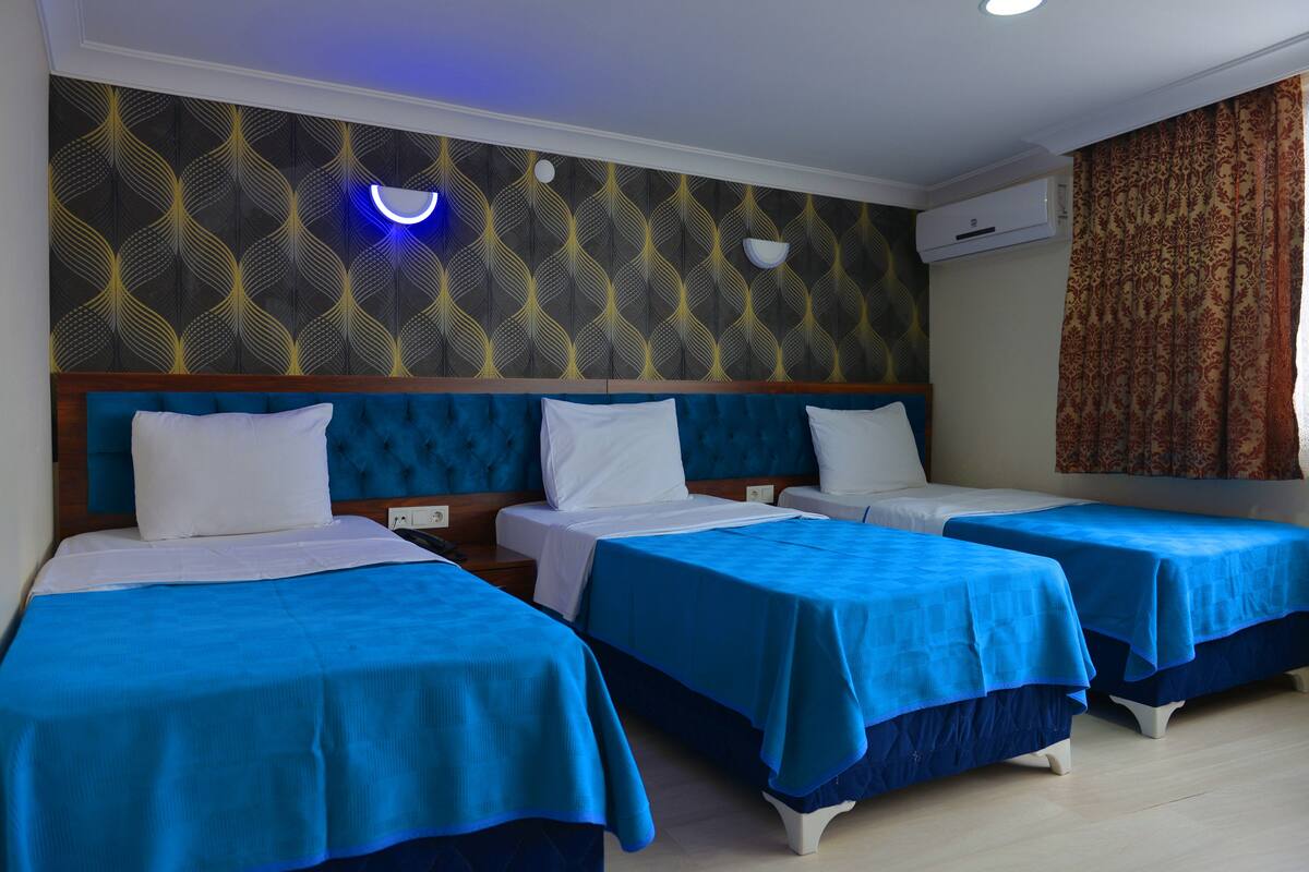A hotel room with three single beds, a modern headboard, a patterned wall, and an air conditioning unit.