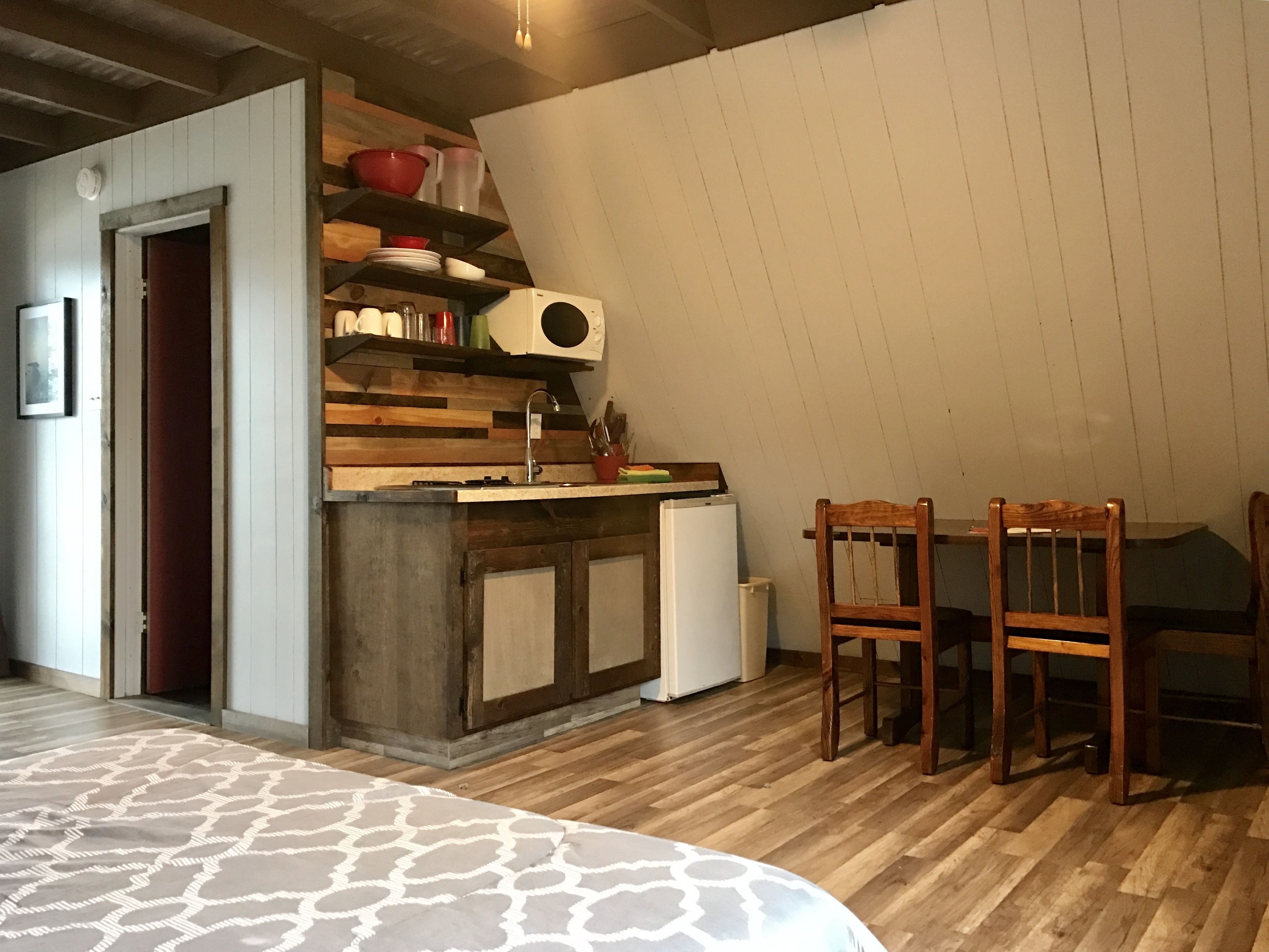 A compact kitchen with a wooden countertop, a sink, and a microwave. There is a dining table with chairs and a patterned rug.