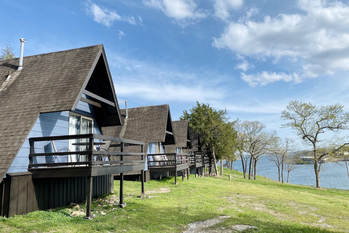 A row of modern cabins with sloped roofs, wooden decks, and large windows overlooking a lake.