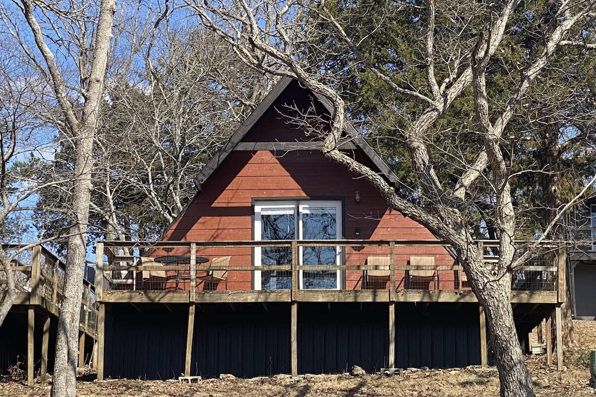 A cabin with a wooden deck, a large window, and a dark exterior.